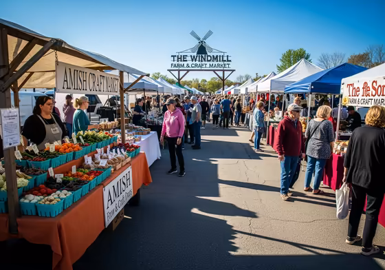 A bustling scene at The Windmill Farm & Craft Market, with vendors under canopies and shoppers browsing fresh produce and handmade crafts.