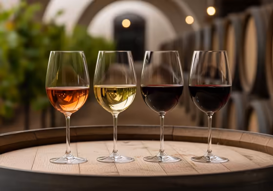 A close-up of a wine tasting flight with several glasses of red and white wine on a rustic wooden barrel.